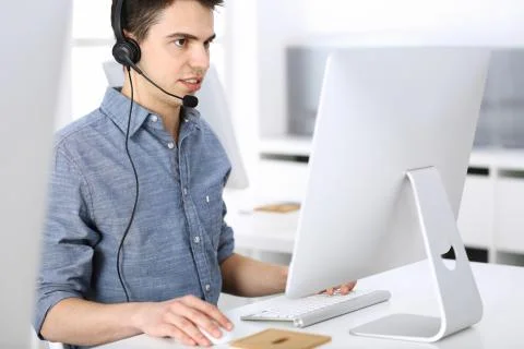 Group of operators at work. Call center. Focus on young man receptionist in Stock Photos