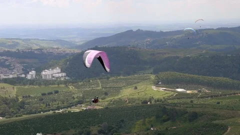 Group of para gliders floating through green open valley with mountain Video stock 101748100