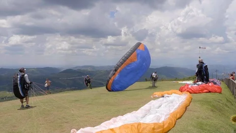 Group of para gliders watching lone pilot prepare &amp; jump off hillside Stockbeeldmateriaal 102064729