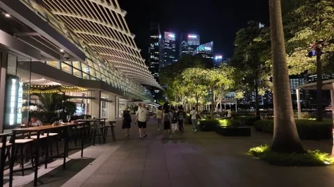 A group of people are walking down a sidewalk in a city near Marina Bay Sand Stock Footage 315682138