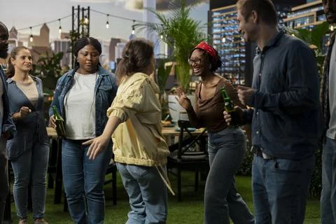 Group of people dance and talk around rooftop barbecue area with drinks Stock Photos