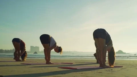 Group of people do standing forward bend pose beach sunset rapid slow motion Stock Footage 84923373