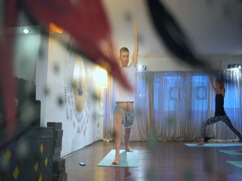 Group of people doing Warrior I Pose, Virabhadrasana I on mats in a yoga studio Stock Footage 70335720