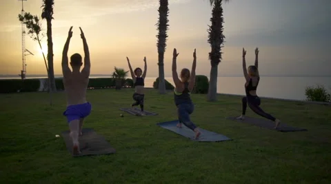 Group of people doing yoga on grass by the sea at dawn slow motion Stock Footage 63050225