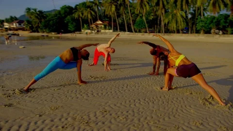 Group of people practicing triangle pose on beach during sunset Stock Footage 75291359