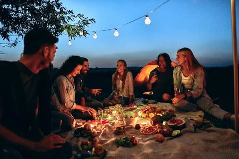 Group people rest near camping tent in evening time Stock Photos