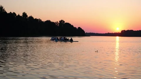 Group of people rowing on long board in lake during golden sunset. Friends Stock Footage 340356893