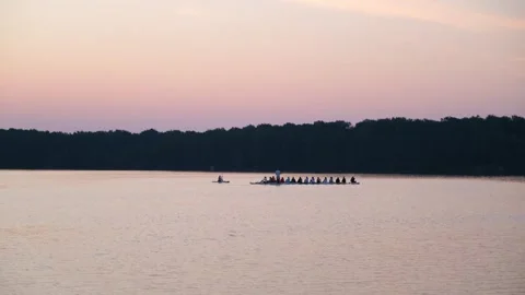 Group of people rowing a long boat across a calm lake at sunset. Team athletes Stock Footage 340356805