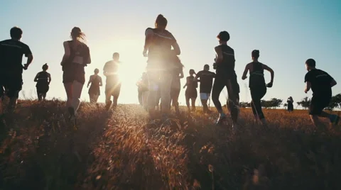 Group of people running on a field in sunset, slow motion Stock Footage