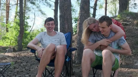 Group of people sitting in a pine forest on camping chairs and laughing. Видео 138148481