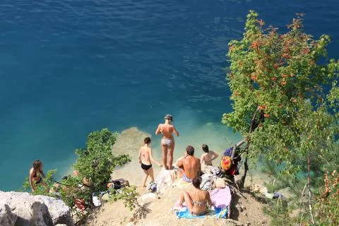 Group of people sunbathing and preparing to swim on a rocky ledge above a cle Stock Photos