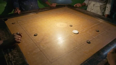 Group playing carrom board game with fast striker movement in night indoor scene 動画素材 332791007