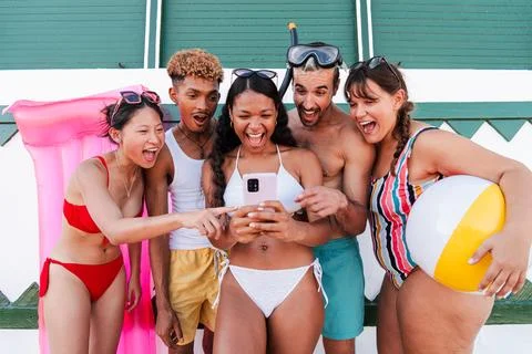 A group of real multiracial friends using a smartphone on the beach. Young Stock Photos