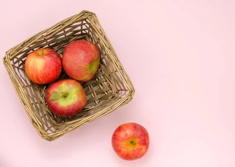 Group of red apples in wicker basket on pink background with copy space. Stock Photos