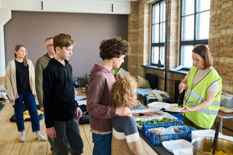 Group of refugees standing in queue in front of table with cooked food Stock Photos