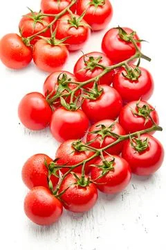Group of ripe cherry tomatoes on branches, on a white wood textured background. Stock Photos