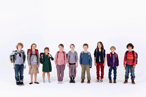 A group of school children wearing backpacks, standing in a row Stock Photos