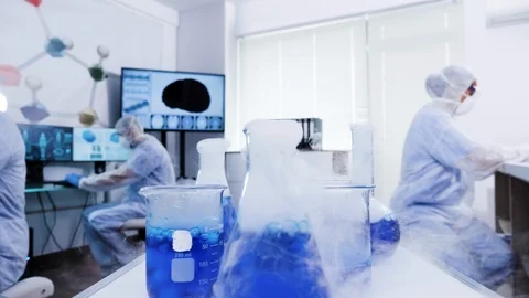 Group of scientist in coverall equipment taking blue smoking liquid from cart Video stock 114559629
