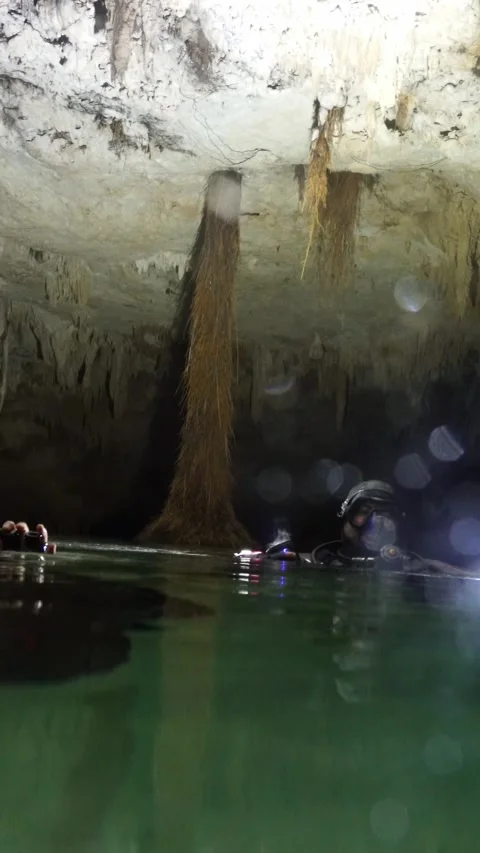 Group of scuba divers emerging in a dark underground cave with stalactites Stock Footage 332001938