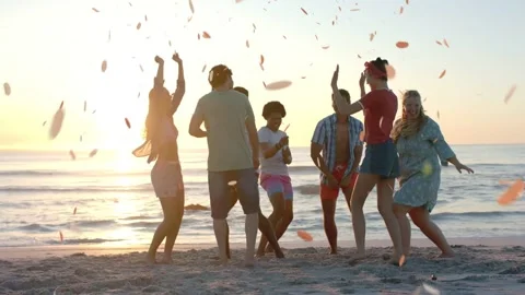 Group of seven adults dancing on beach at sunset, petals falling around group Stock Footage 337913029