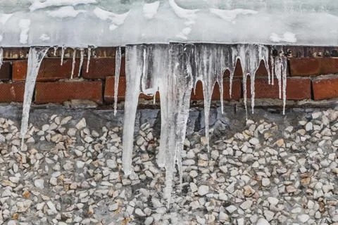 A group of sharp white transparent icicles is hanging down from the gray roof Stock Photos