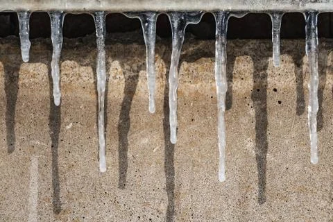 A group of sharp white transparent icicles with shadows is hanging down from Stock Photos