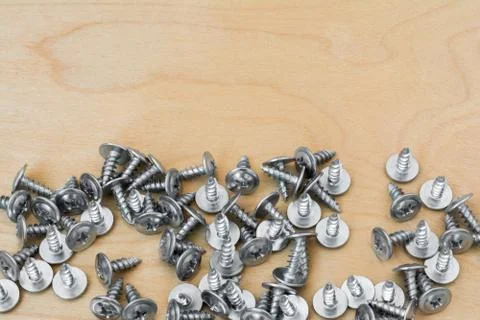 Group of silvery self-tapping screws is arbitrarily positioned on a wooden su Stock Photos