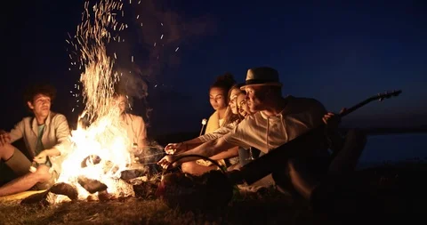 Group of six old multi-ethnic friends sitting near bonfire, roasting sausages Stock Footage 94723037