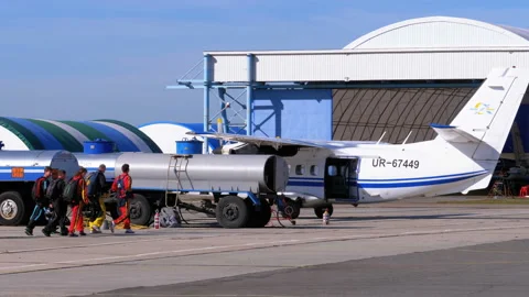 Group of skydivers goes to the plane parked near the hangar on a small airfield Stock Footage 96506670