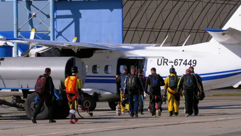 Group of skydivers goes to the plane parked near the hangar on a small airfield Stock Footage 96524931