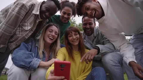 Group smiling college outdoors using cell phone. Cheerful yellow girl holds 库存影片 252086883