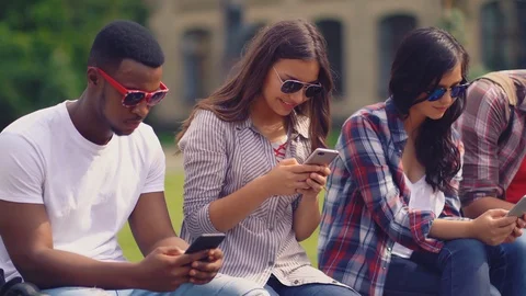 Group of smiling friends looking at cell phones outdoors Stock Footage 126287553