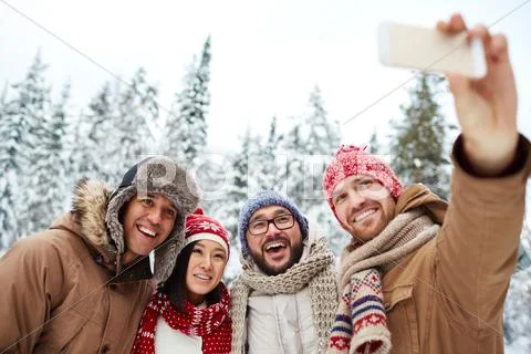 Group of smiling men and woman taking selfie with mobile phone in winter forest Stock Photos