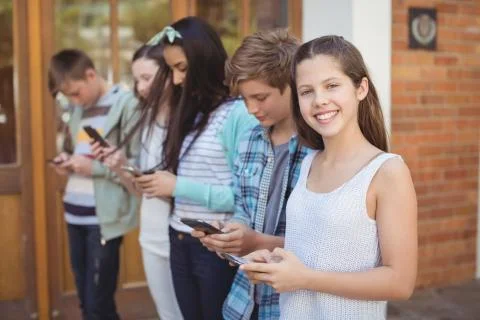Group of smiling school friends using mobile phone in corridor 스톡 사진