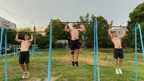 Group of strong sporty men doing pull ups on horizontal bar at sports ground. Yo Stock Footage 335818007