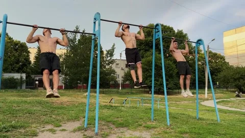 Group of strong sporty men doing pull ups on horizontal bar at sports ground. Yo Stock Footage 338130506