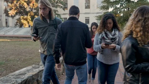 Group of students all on their mobile phones walking and ignoring each others Видео 104364562