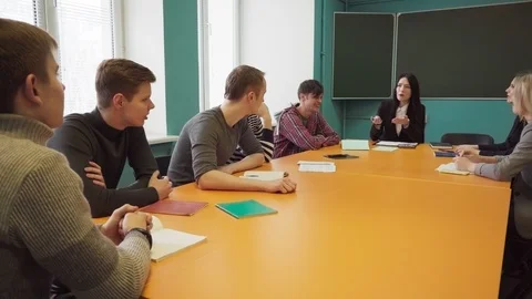 Group of students and a teacher sit at a table and talk Stock Footage 86493848