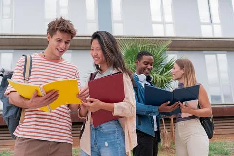 Group of students outside the campus talking and sharing notes holding notebooks Stock Photos