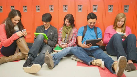 A group of students sit against lockers and play with their phones and tablets Stock Footage 33890643