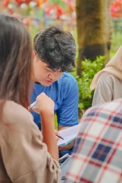 Group of students is sitting in the park, the man is writing in a notebook. Stock Photos