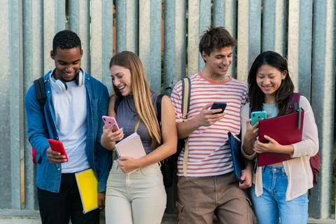 Group of students standing outside the campus using the smartphones watching Stock Photos