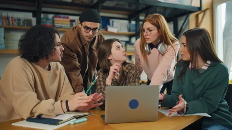 Group of students studying together in a library while looking at a laptop and d Stock Footage 337324869
