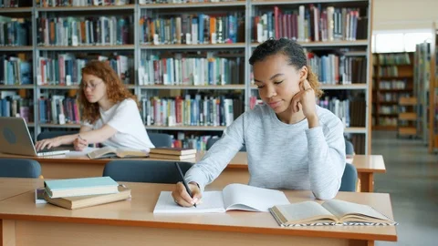 Group of students working in library reading books writing studying indoors Stock Footage