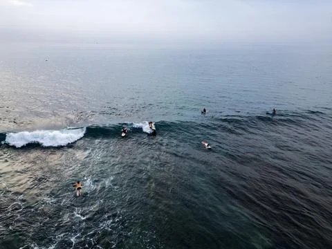 A group of surfers catching waves in the open ocean under a cloudy sky. Aeria Фото