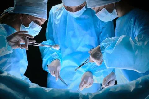 Group of surgeons at work in operating theater toned in blue Фото