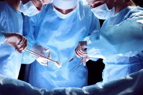 Group of surgeons at work in operating theater toned in blue Фото