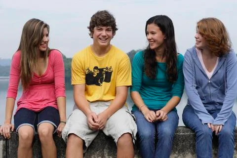 Group of teens sitting on wall next to lake Stock Photos