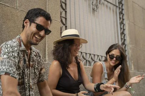 A group of three friends having fun and laughing on a bench in the street Stock Photos