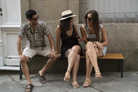 A group of three friends having fun and laughing on a bench in the street Stock Photos